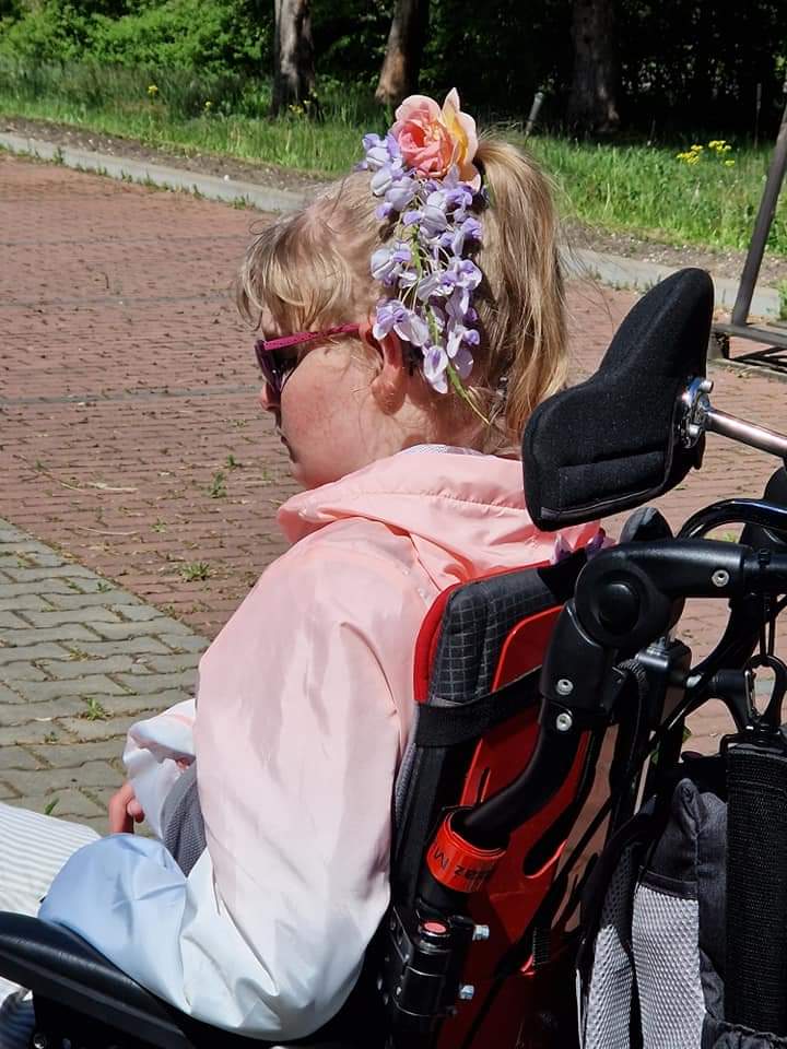 dziewczynka na wózku inwalidzkim z kwiatami we włosach