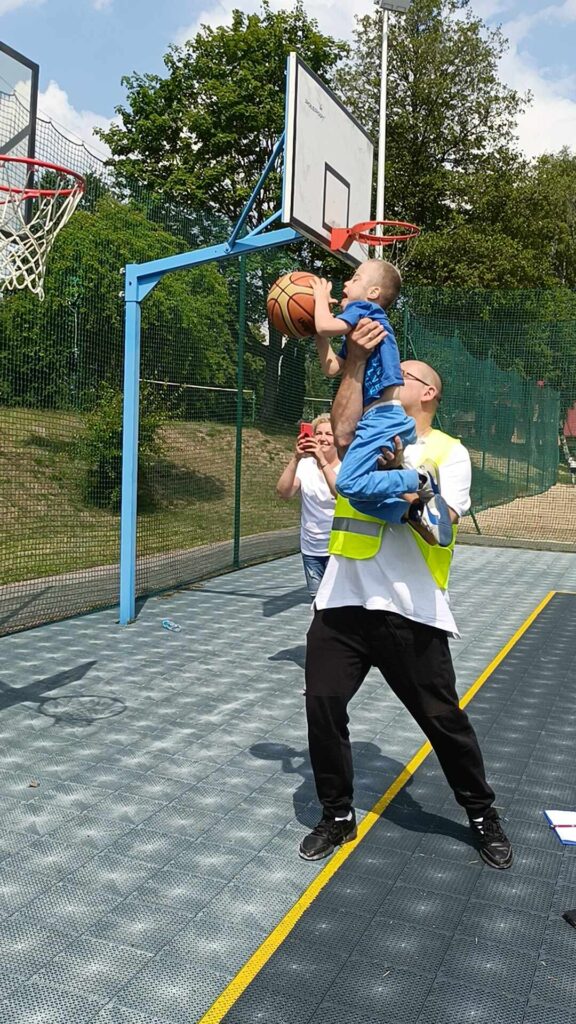 mężczyzna trzymający na rękach chłopca z zespołem downa. chłopiec trzyma piłkę do kosza