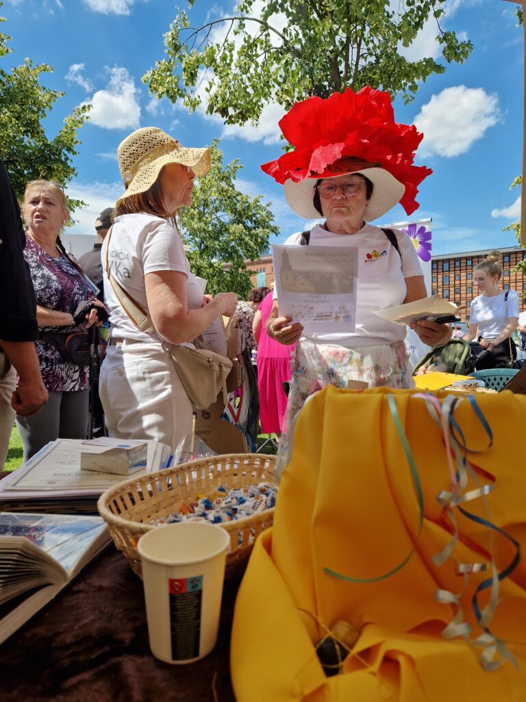 ludzie i kobieta w kapeluszu z wielkim czerwonym kwiatem na nim 