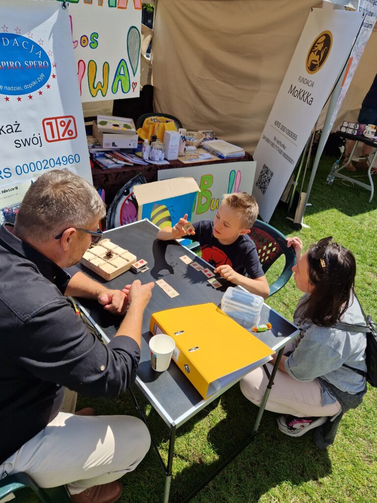 chłopiec z mamą i mężczyzna grający w domina z kartonu przy stoisku fundacji mokkka