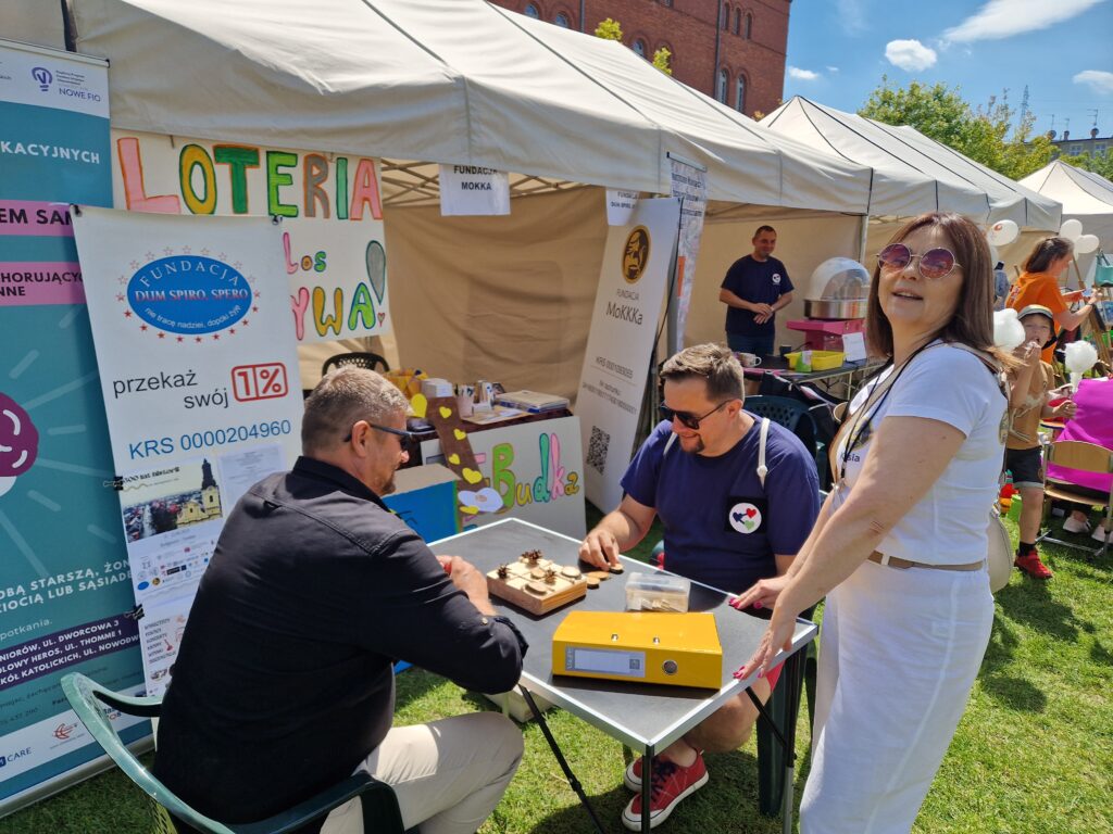 namioty stoiska i dwóch mężczyzn grających w eko kółko i krzyżyk z szyszek i drewienek oraz fundatorka Kasia